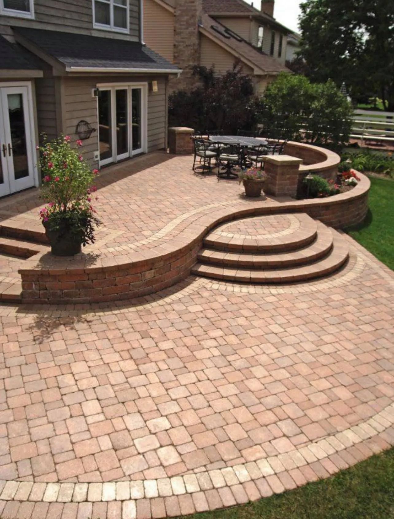 Brick patio with curved stone steps, raised seating wall, and a house in the background