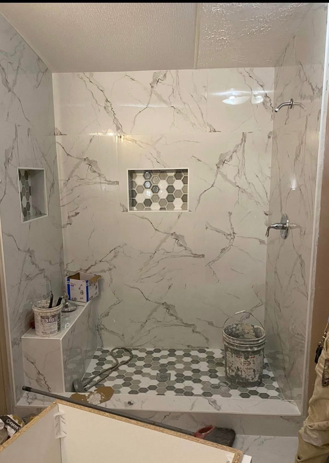 Marble-tiled shower stall with a built-in niche, mosaic floor, and bathroom items on a ledge