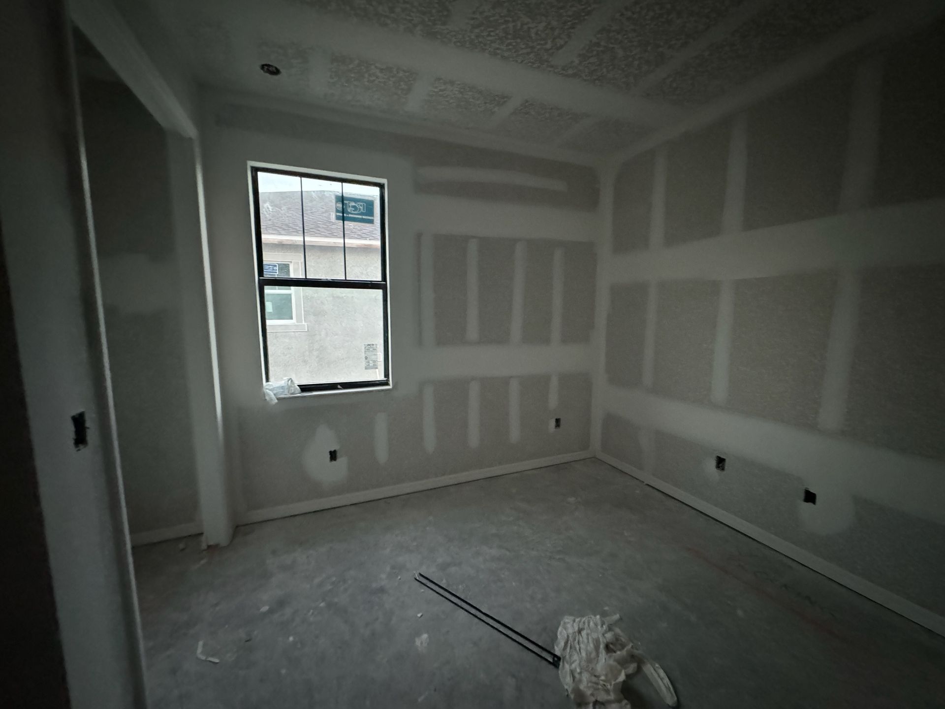 Empty unfinished room with drywall, window, and construction debris on the floor