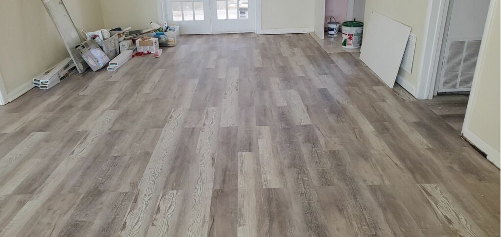 Empty room with light wood flooring, white walls, and scattered renovation supplies along the left side.