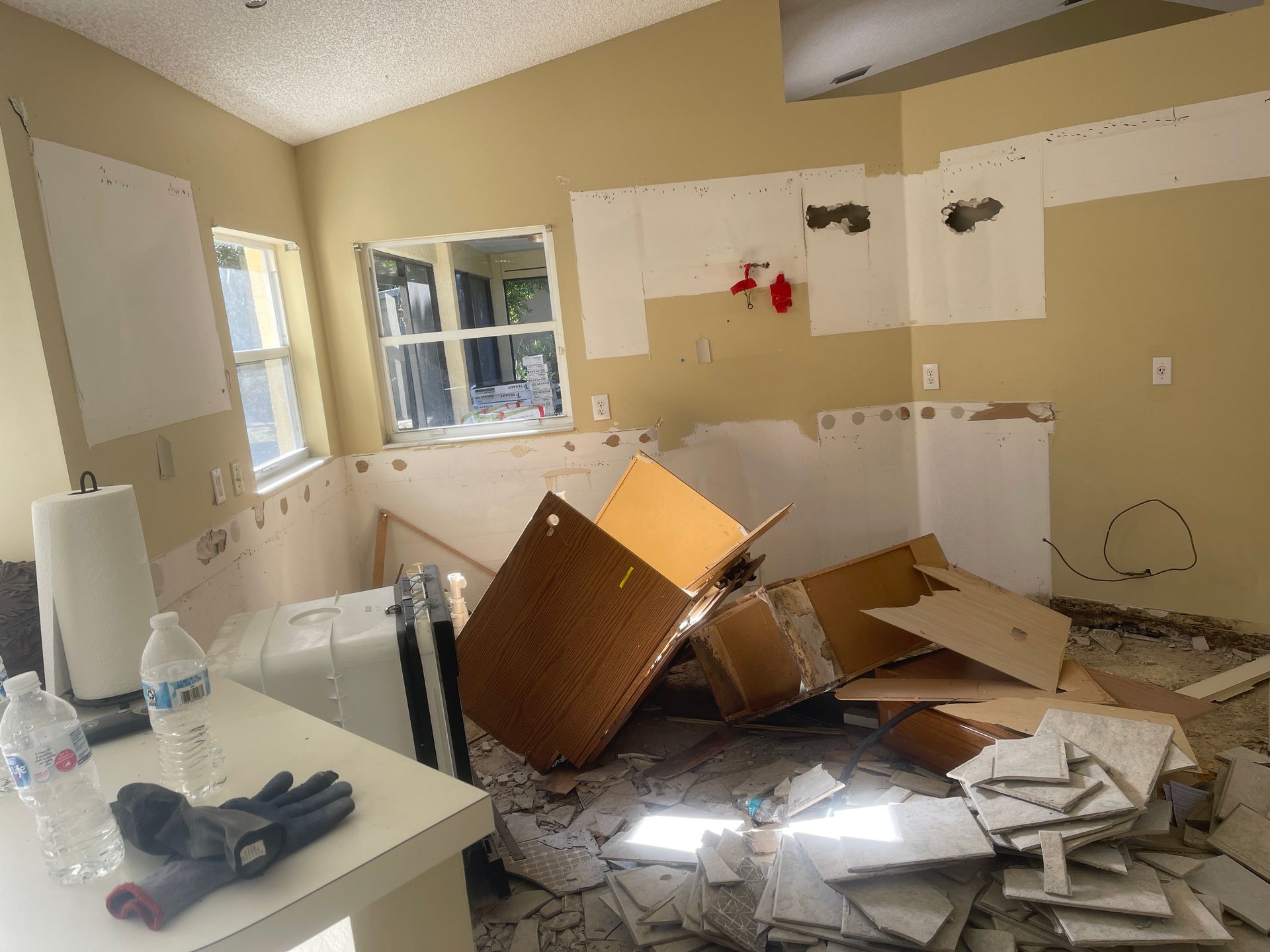 Damaged kitchen with debris, broken cabinets, and scattered rubble after apparent water or fire damage