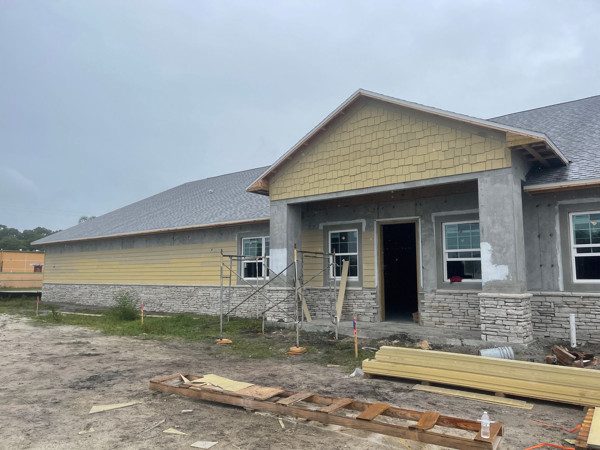 Unfinished house with stone and yellow siding, open doorway, and construction materials in front