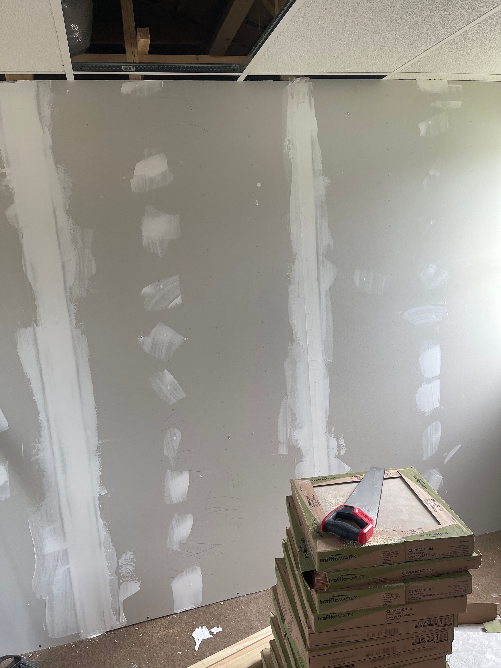 Unfinished room with gray drywall and joint compound; stack of drywall sheets and a tape measure in the foreground
