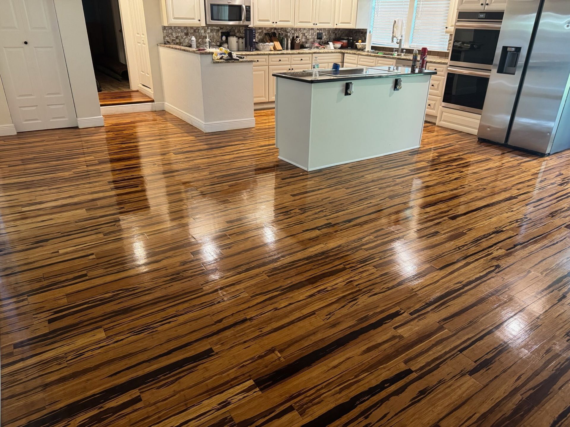 Bright kitchen with glossy patterned hardwood floors and a white island under stainless steel appliances