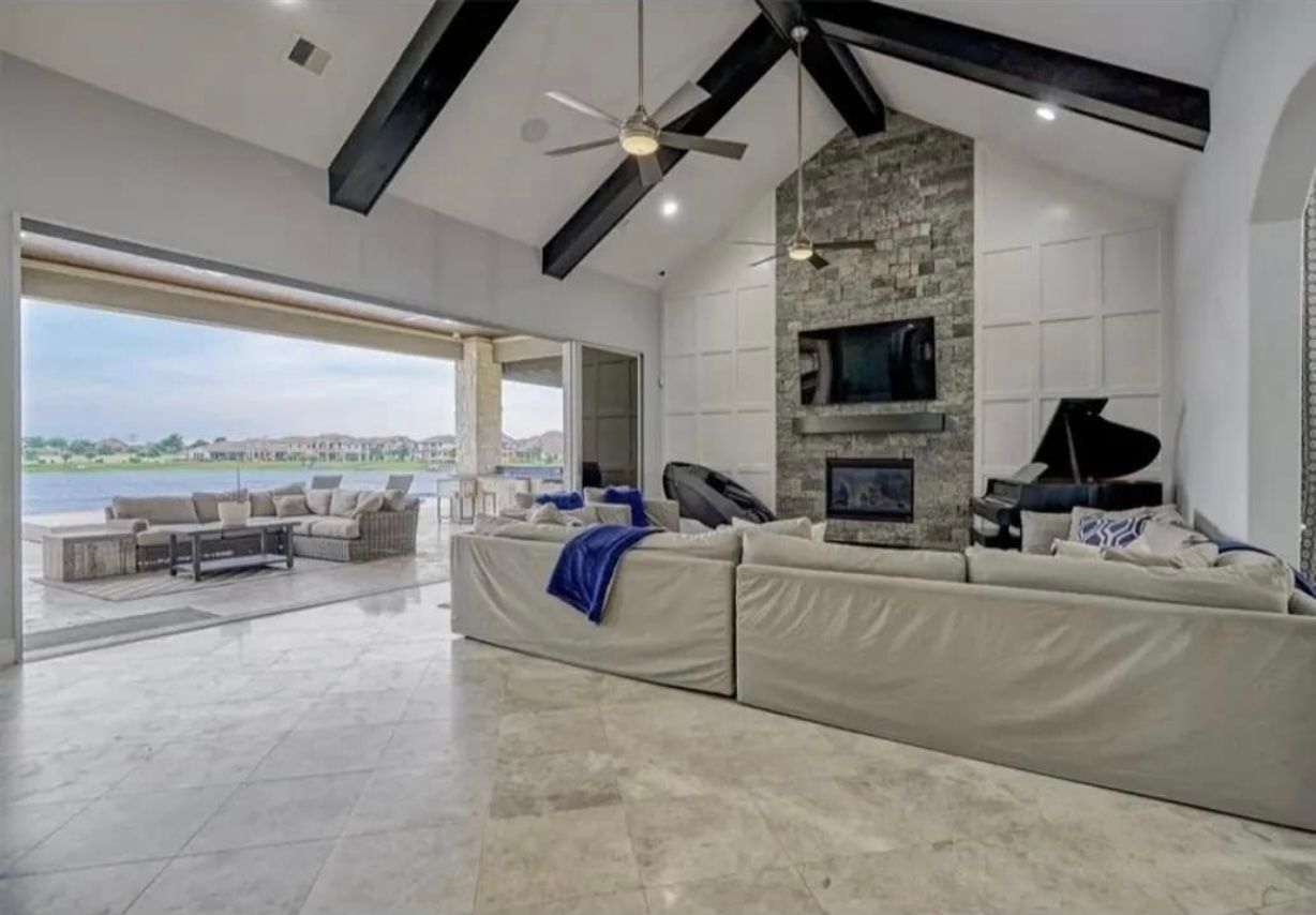 Modern open-concept living room with vaulted ceiling, stone fireplace, and waterfront view through sliding doors