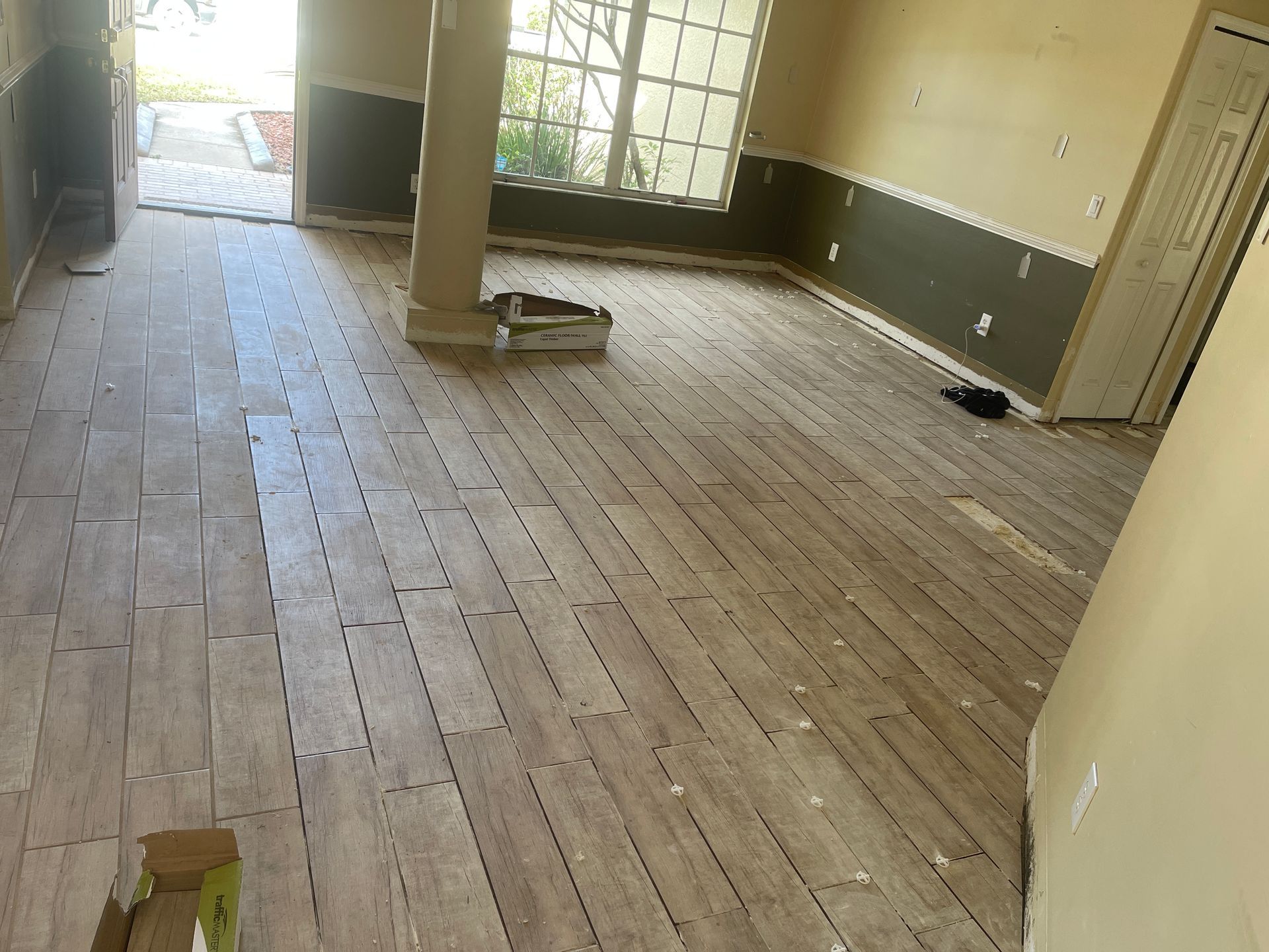 Empty room with unfinished wood floor, exposed pillar, and sunlight through large windows.