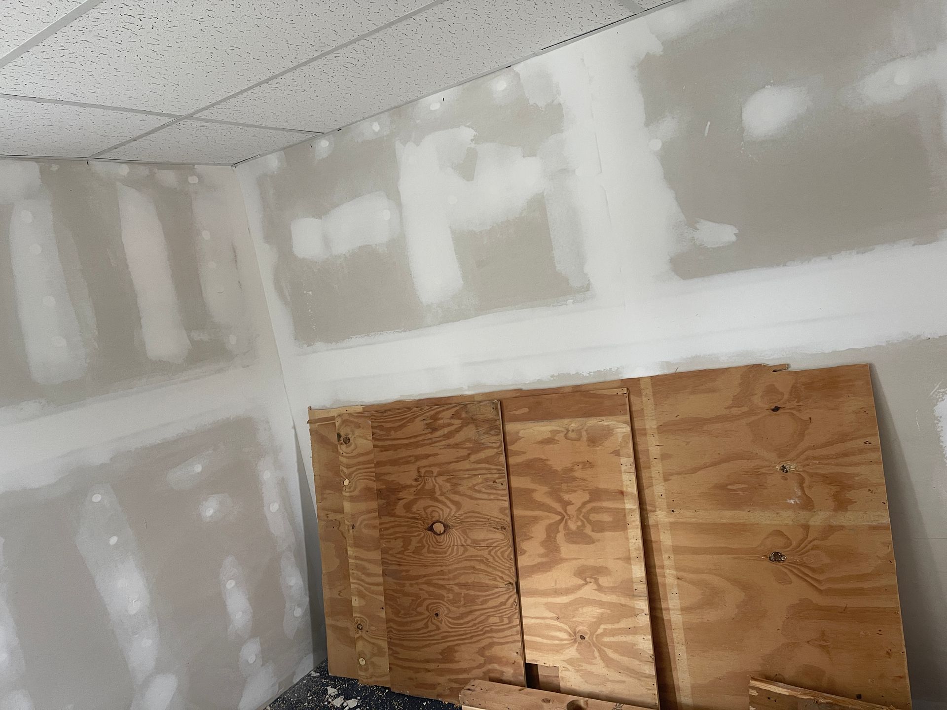 Unfinished drywall room with taped seams and plywood leaning against the wall