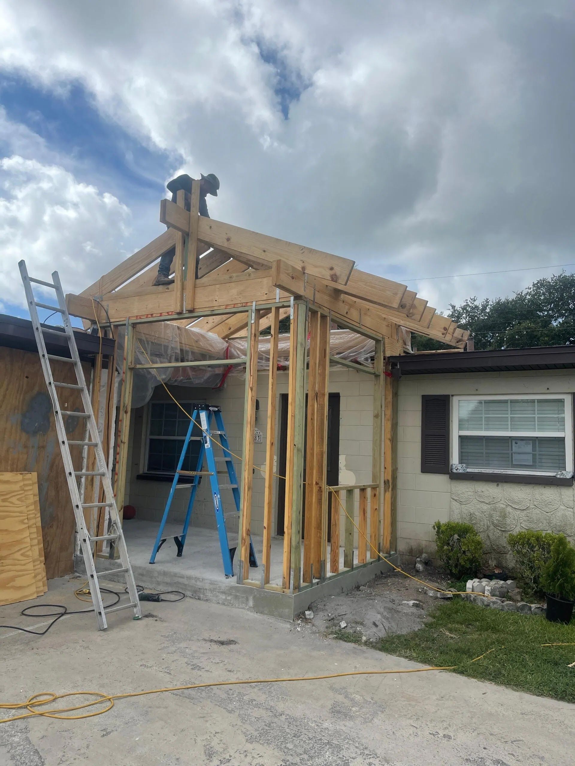 House under construction with wood framing, ladders, and debris beside an attached garage under cloudy skies