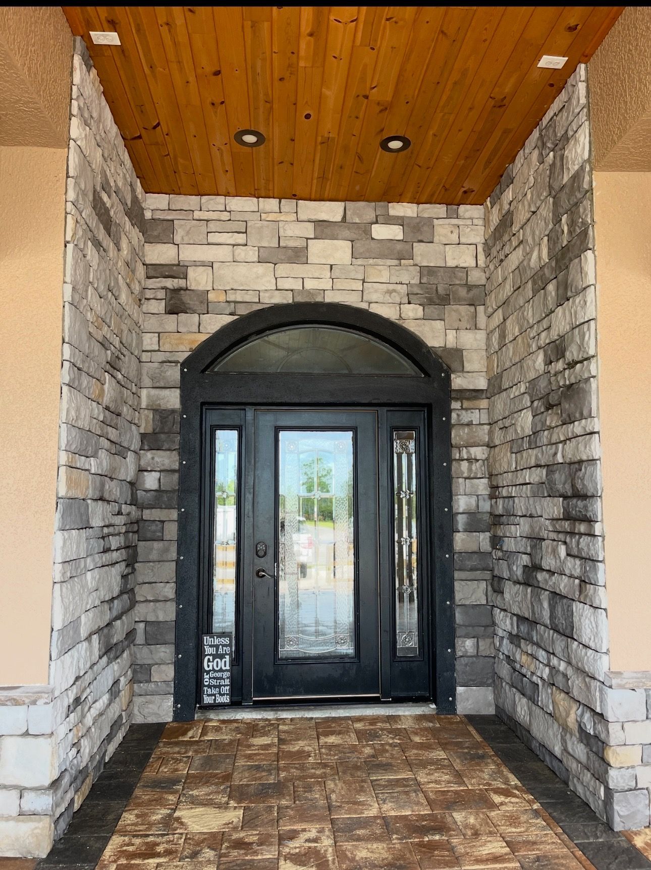 Stone-front entryway with black double doors and a wood-paneled ceiling over a tiled porch
