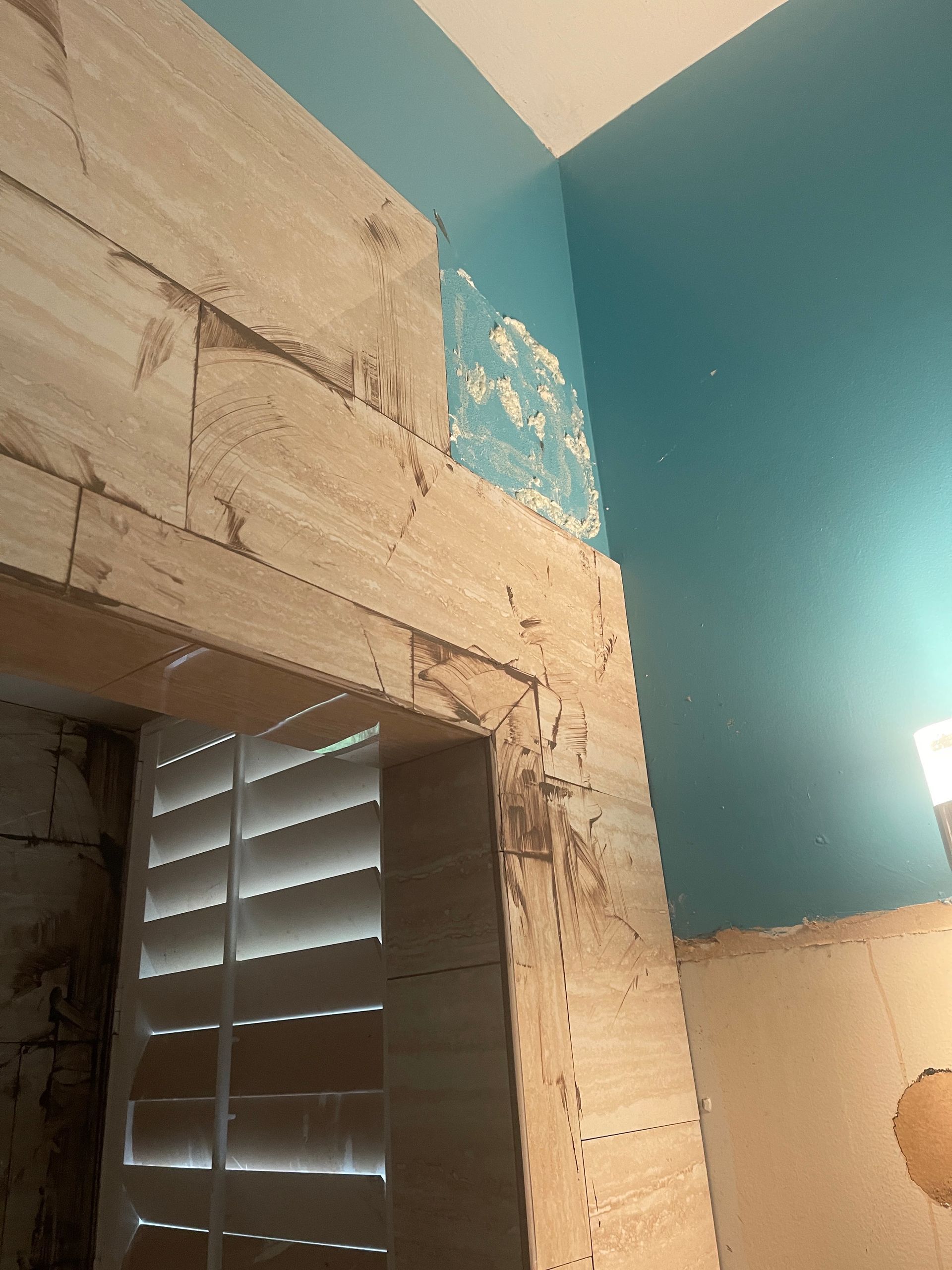 Corner of a room with peeling beige paint, teal walls, and a window with closed blinds.