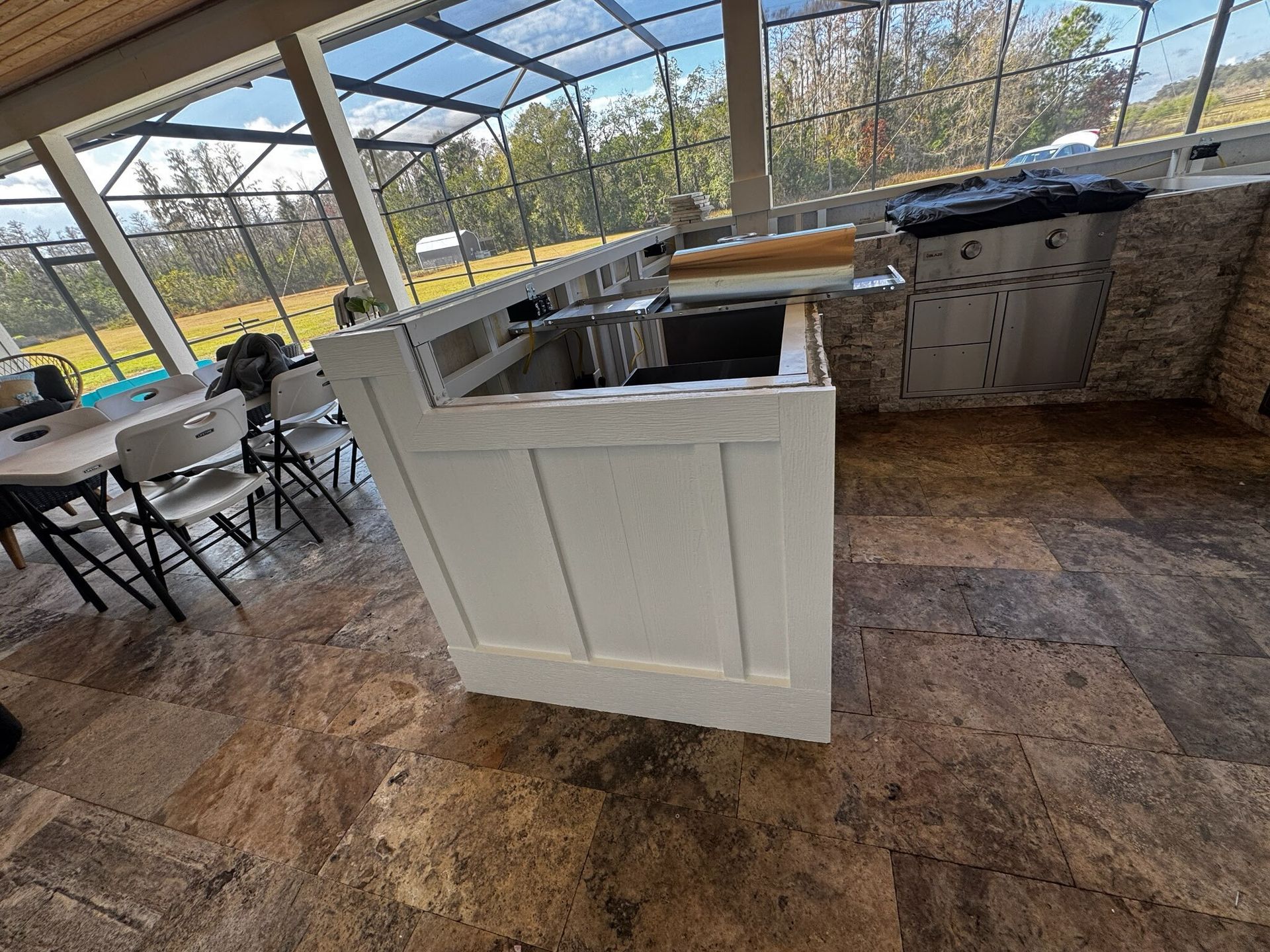 Empty kitchen island in a bright screened patio with tables and cabinets nearby