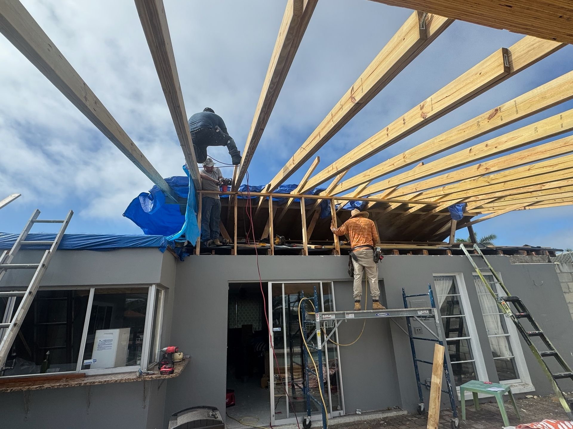 Two workers installing roof beams on a building under construction, with ladders and scaffolding below.