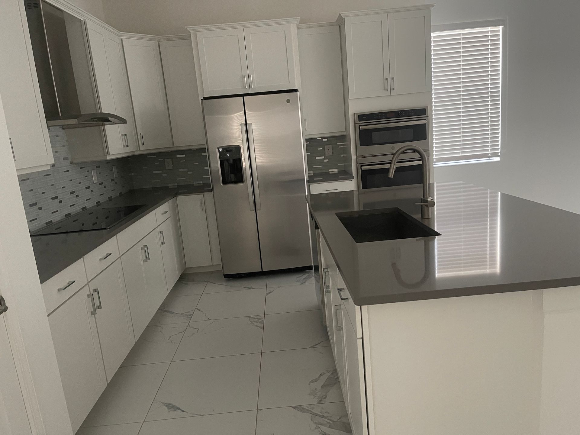 Modern white kitchen with stainless steel refrigerator, tiled floor, and a black sink island.