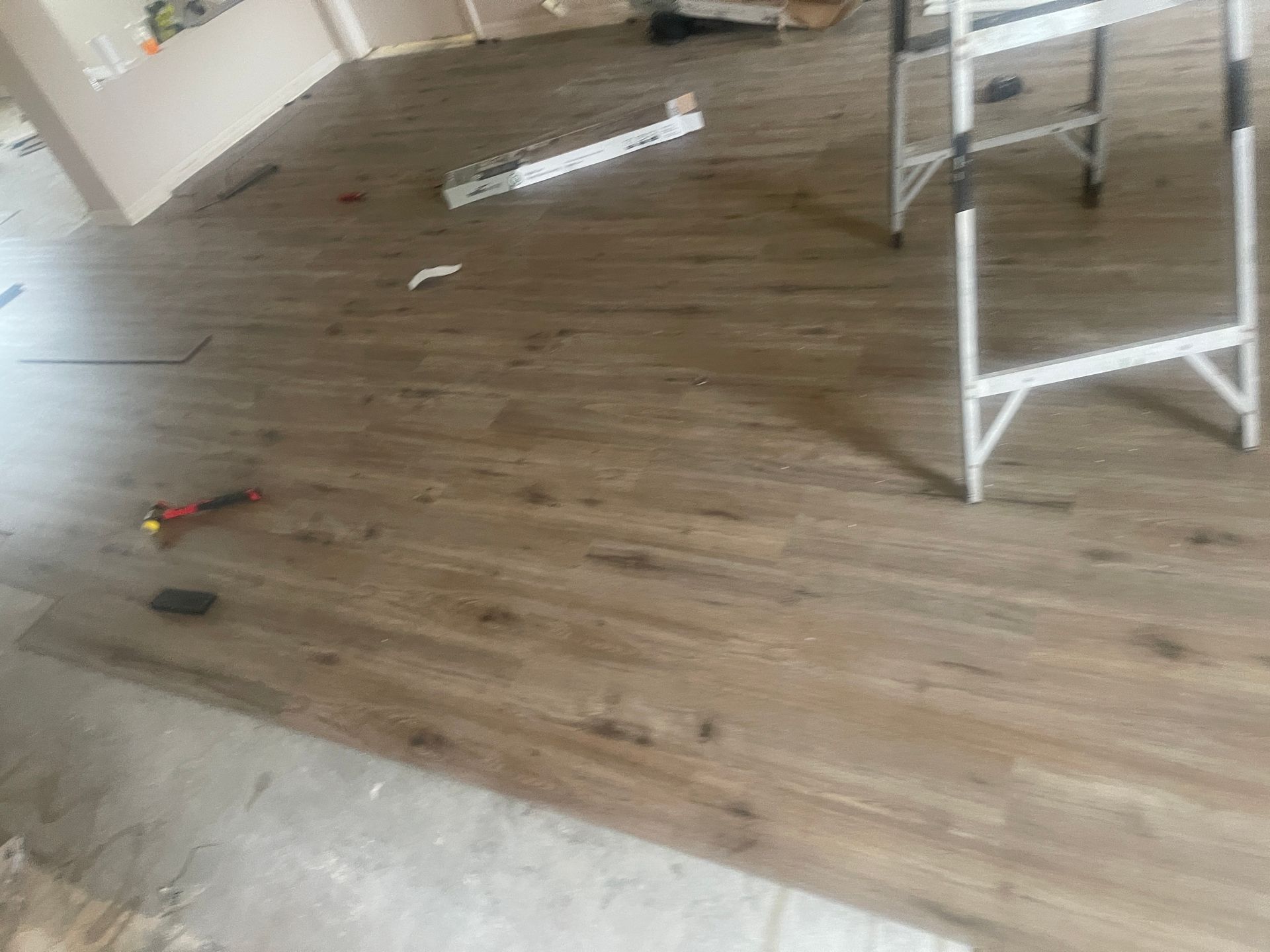 Messy room with wood flooring, scattered tools, and a white chair frame near the right side.