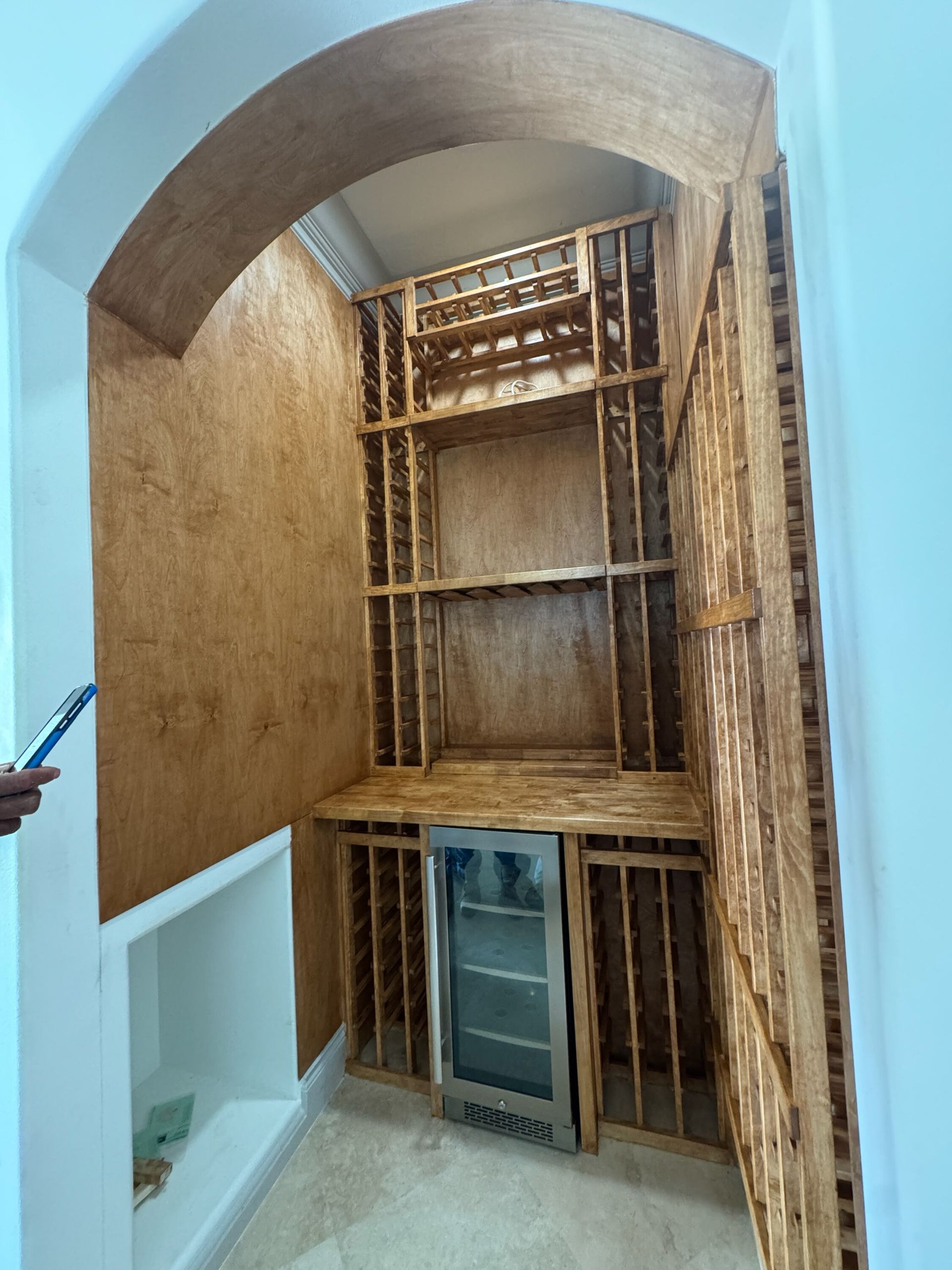 Built-in wooden cabinet alcove with shelving and a small door under an arched ceiling.