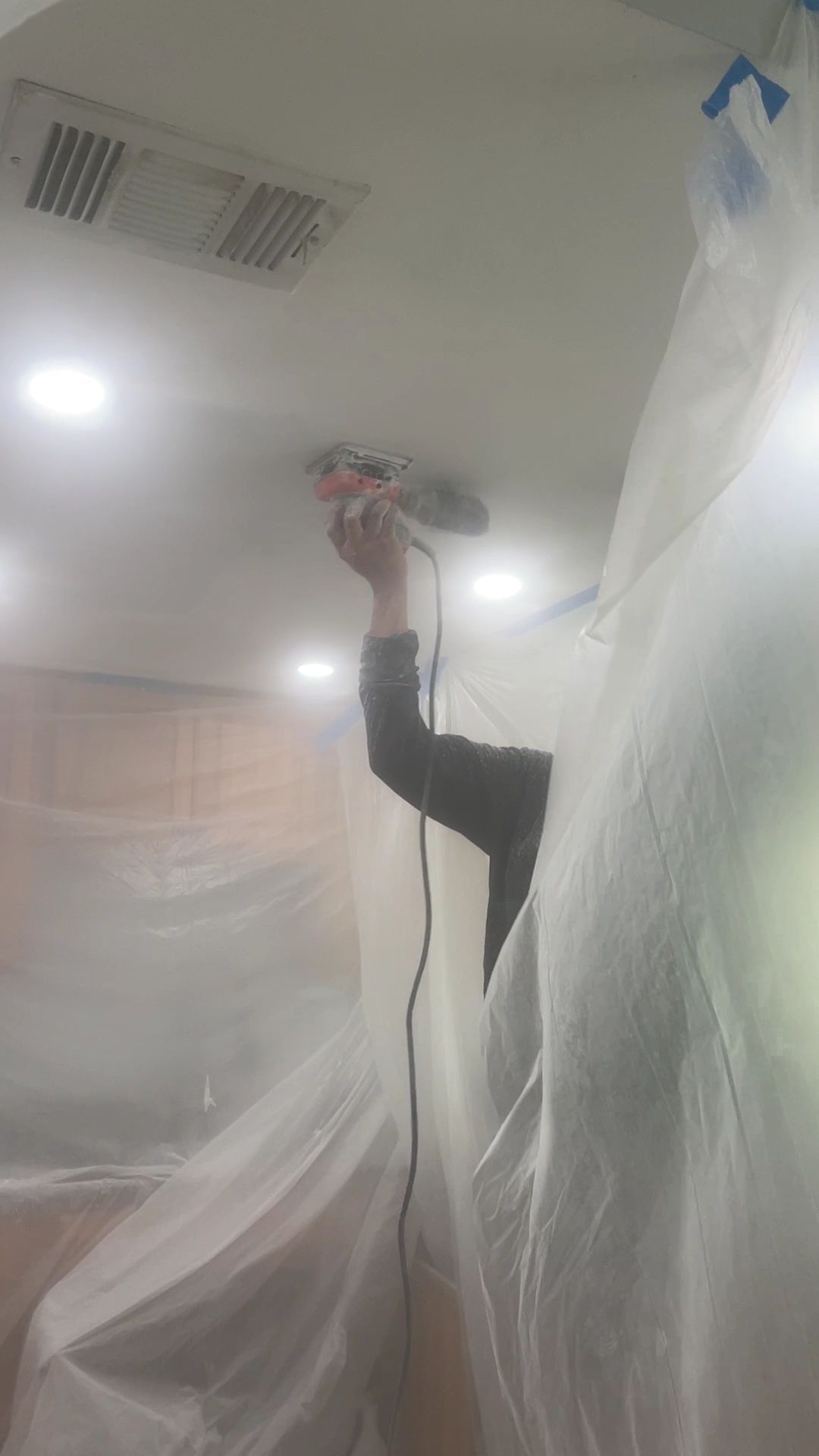 Person spraying paint on a ceiling, with rooms covered in plastic sheeting.