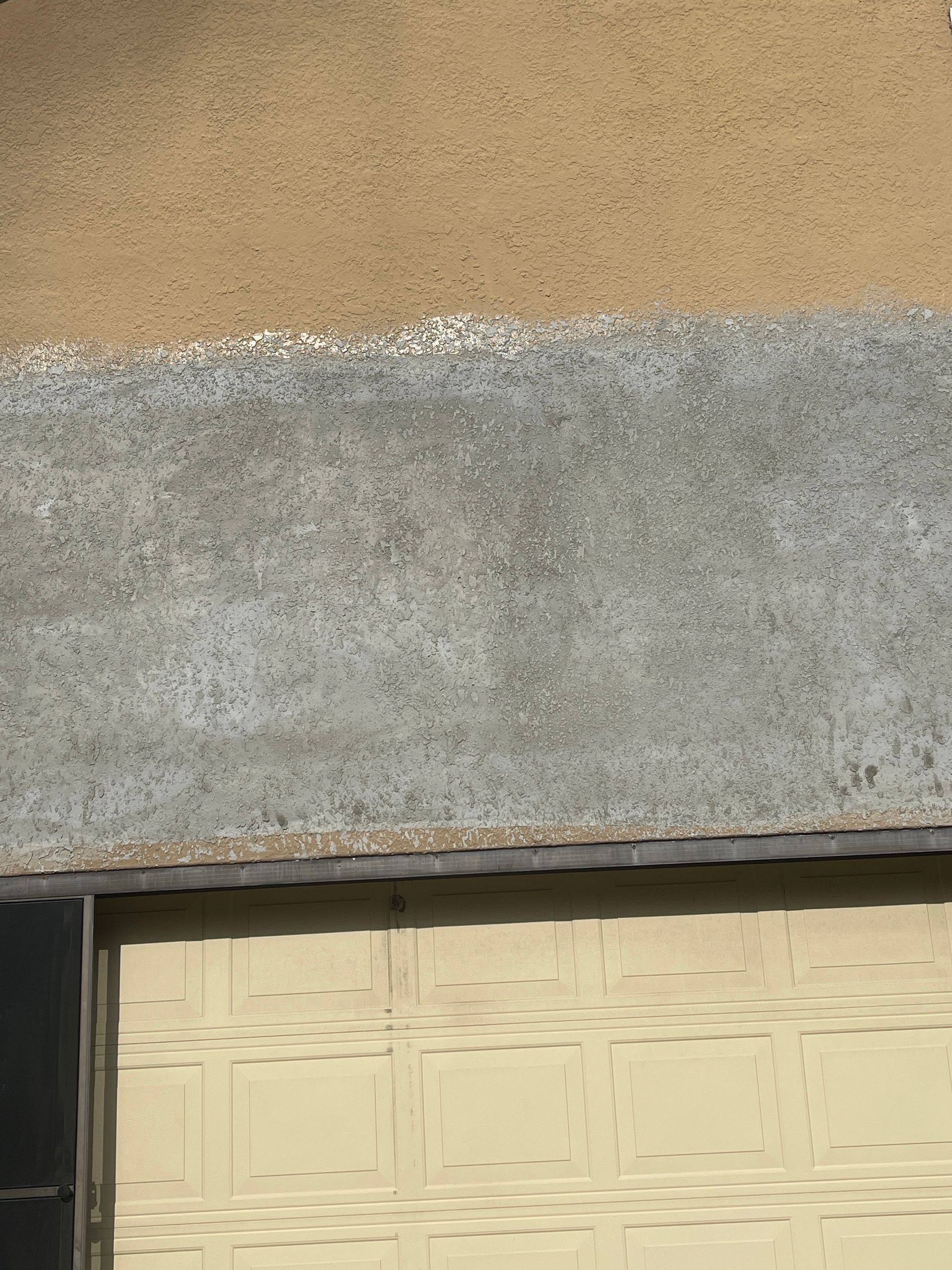 Close-up of a weathered stucco wall above a cream-colored garage door.