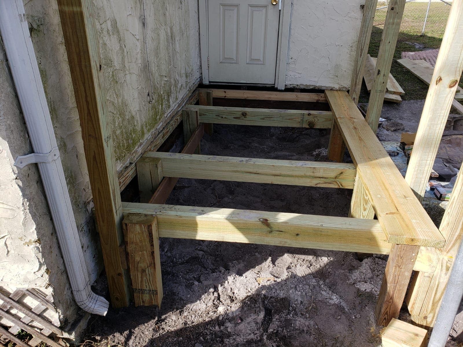 Wooden ramp framing beside a house doorway, with steps removed and soil exposed.