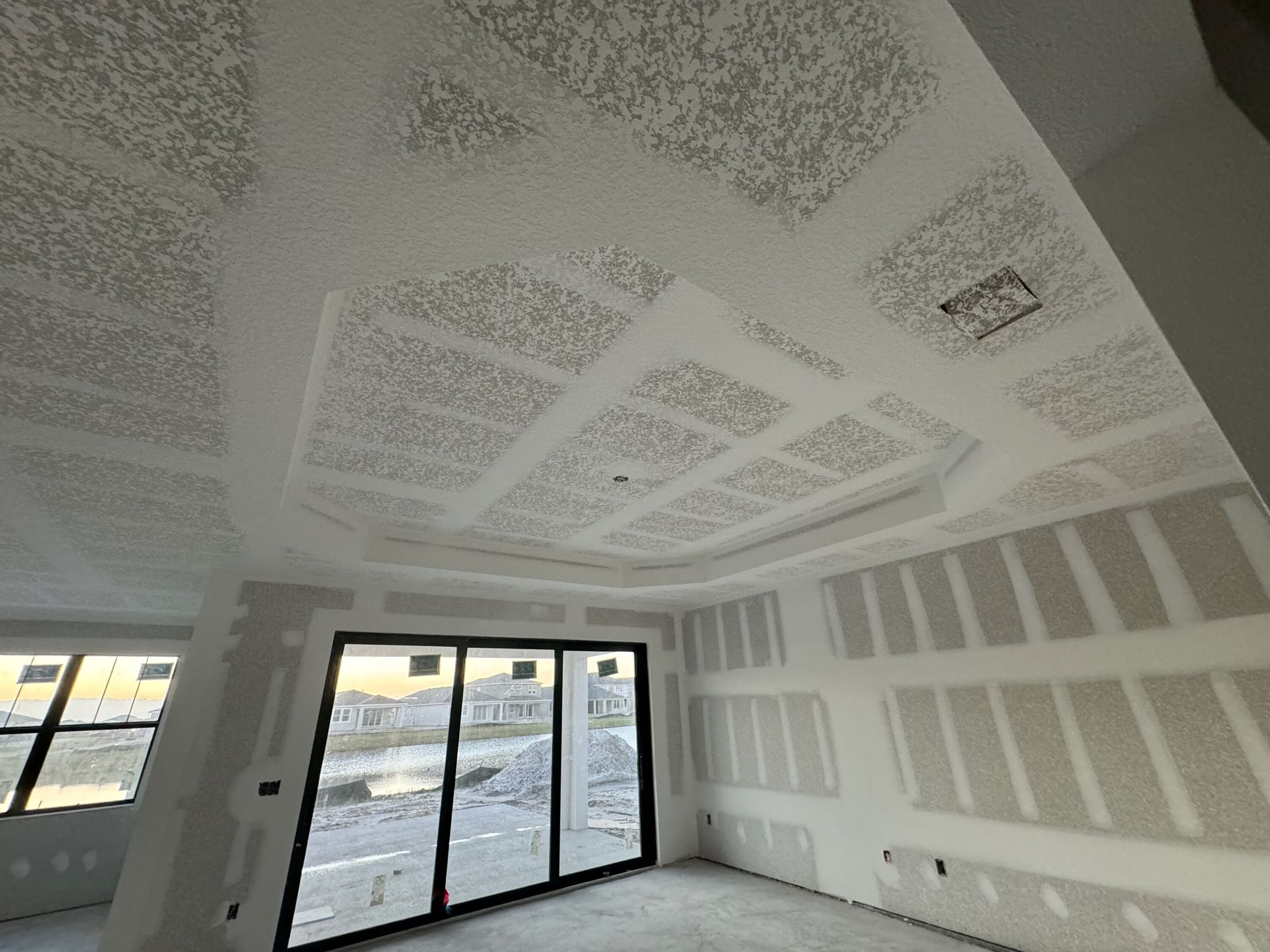 Unfinished room with white drywall, taped seams, and large sliding glass doors letting in daylight.