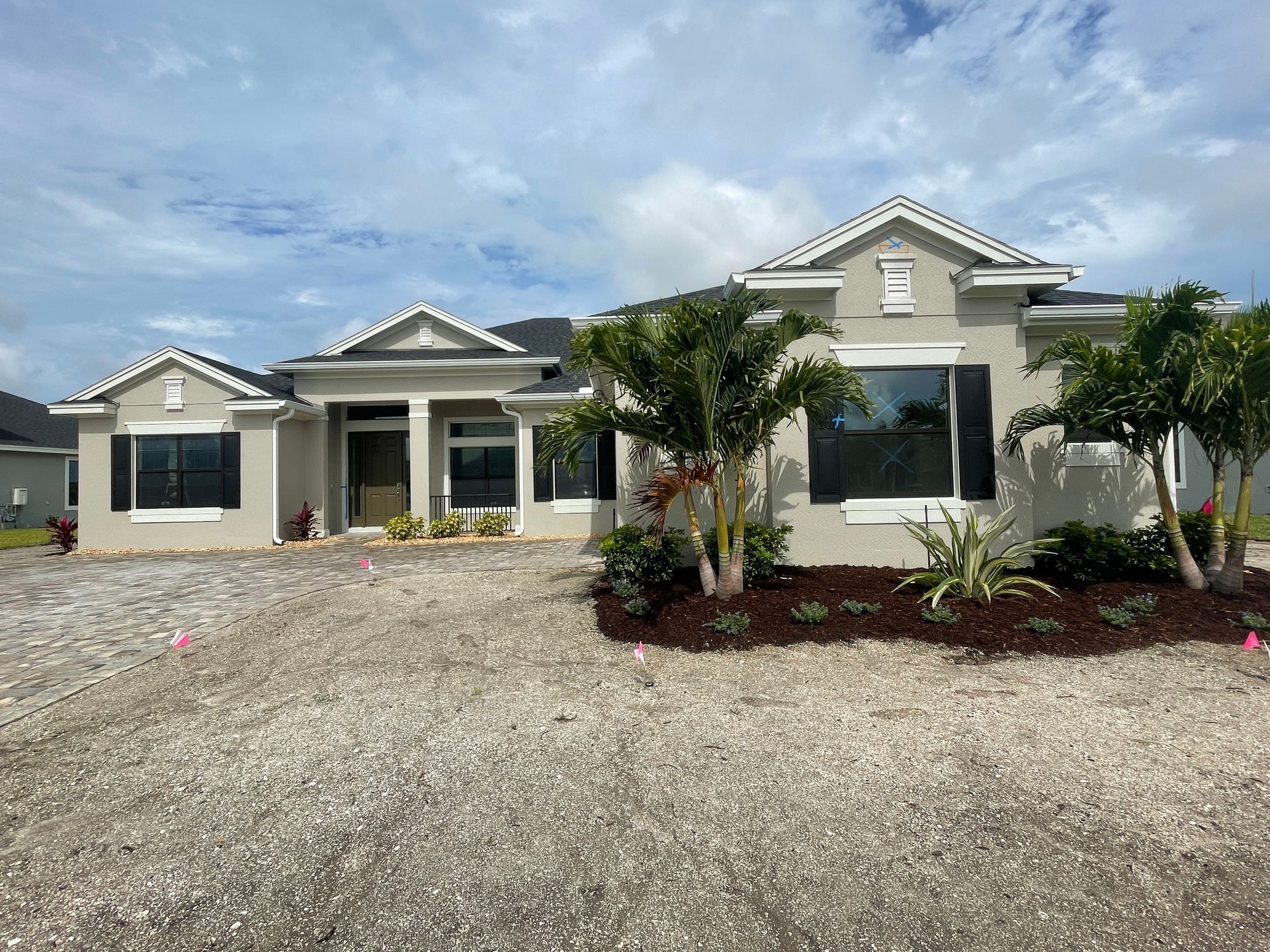 Single-story white house with front porch, gravel driveway, and small landscaped palms under a clear sky