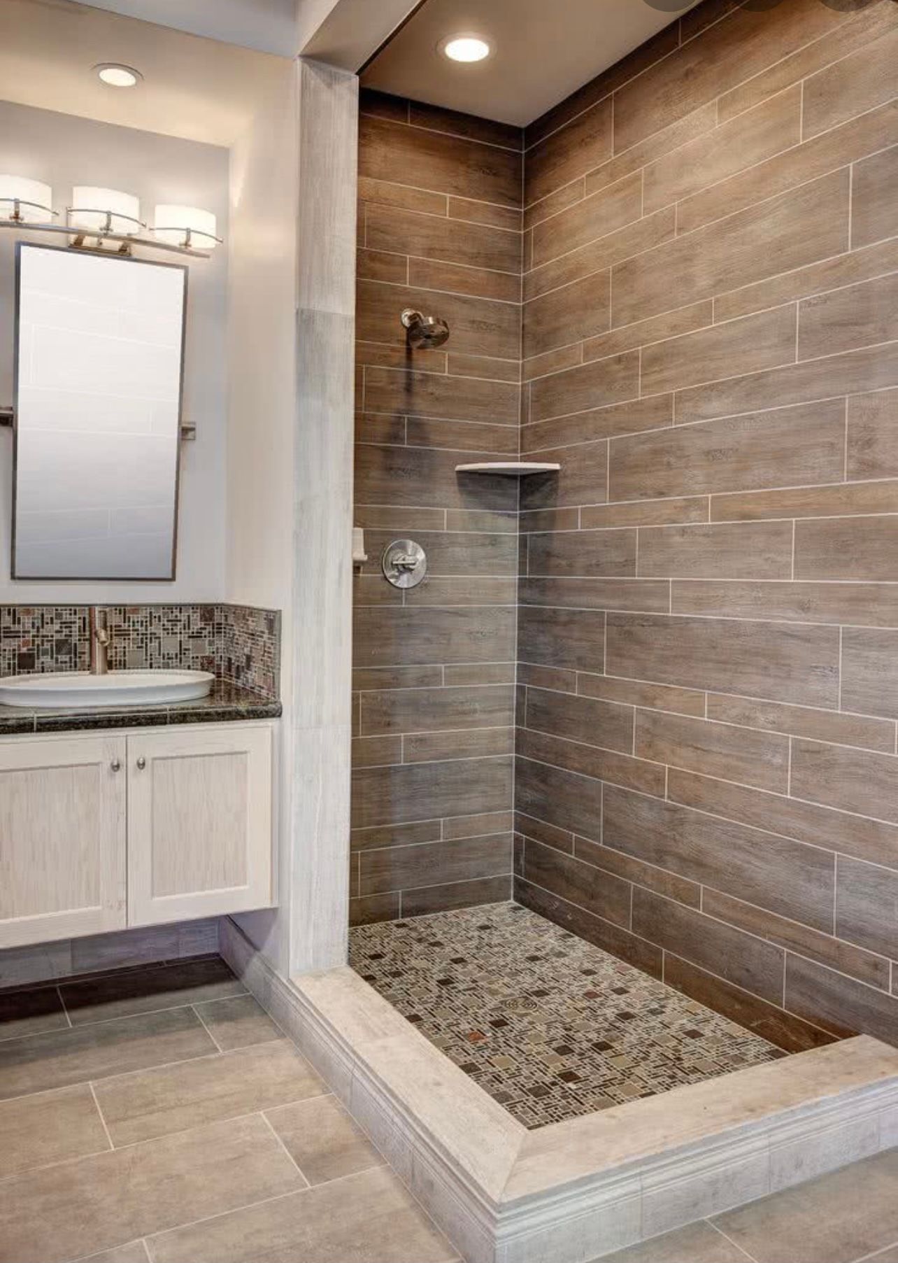 Modern bathroom shower with brown tile, glassless open entry, and adjacent vanity mirror.