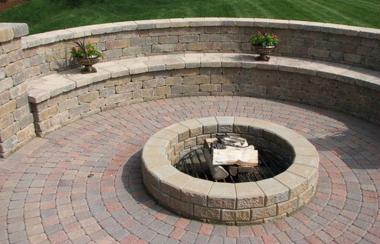 Circular brick fire pit in a stone patio with curved built-in bench seating.