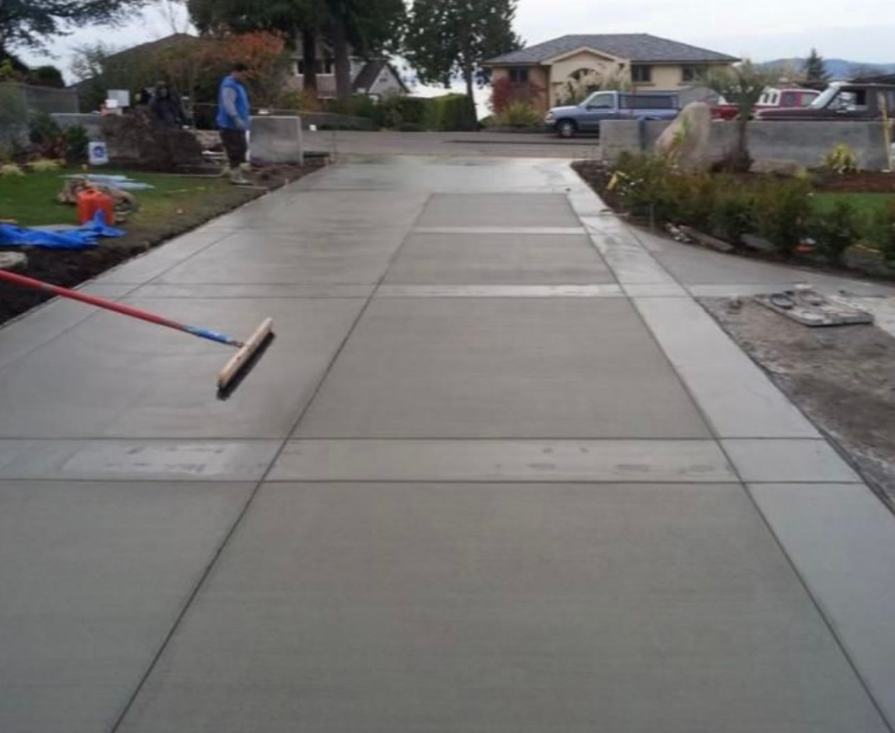 Freshly poured concrete driveway with a long-handled broom on it in a suburban front yard