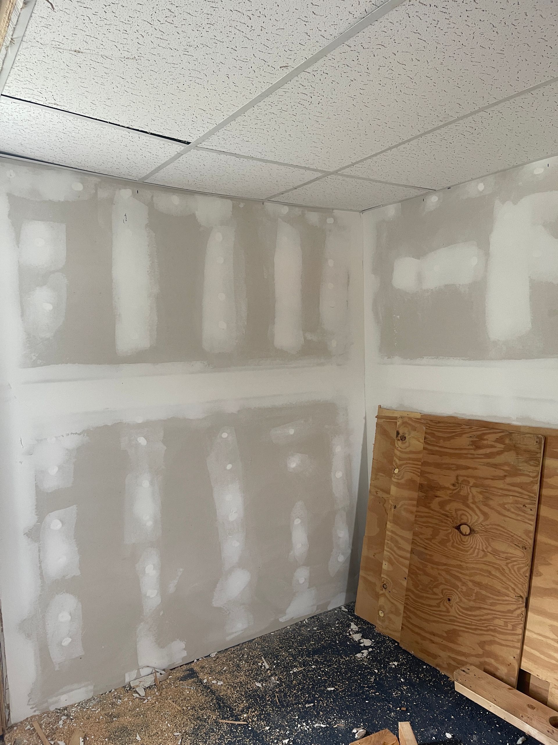 Small unfinished drywall room with taped seams, speckled ceiling, and a wooden crate on the floor.