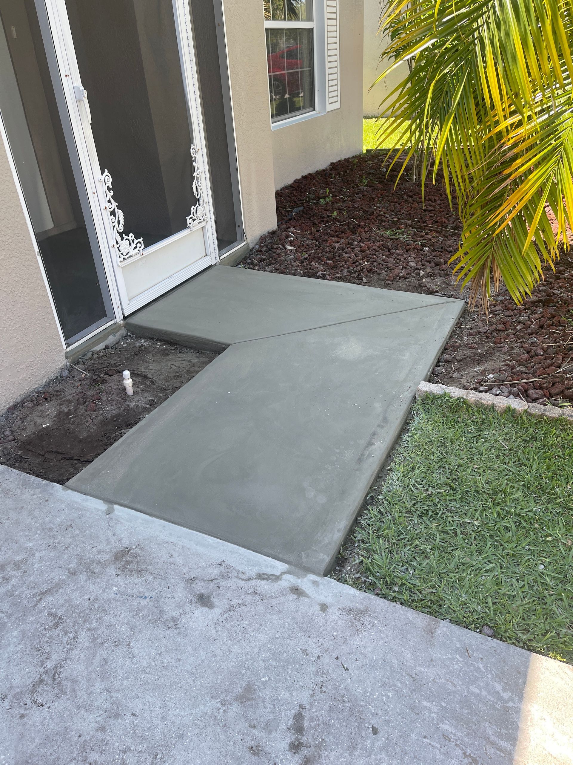 Front entry walkway with a concrete accessibility ramp leading to a door, bordered by mulch and grass.