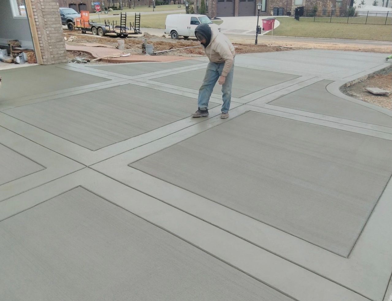 Worker smoothing fresh concrete sidewalk panels at a construction site
