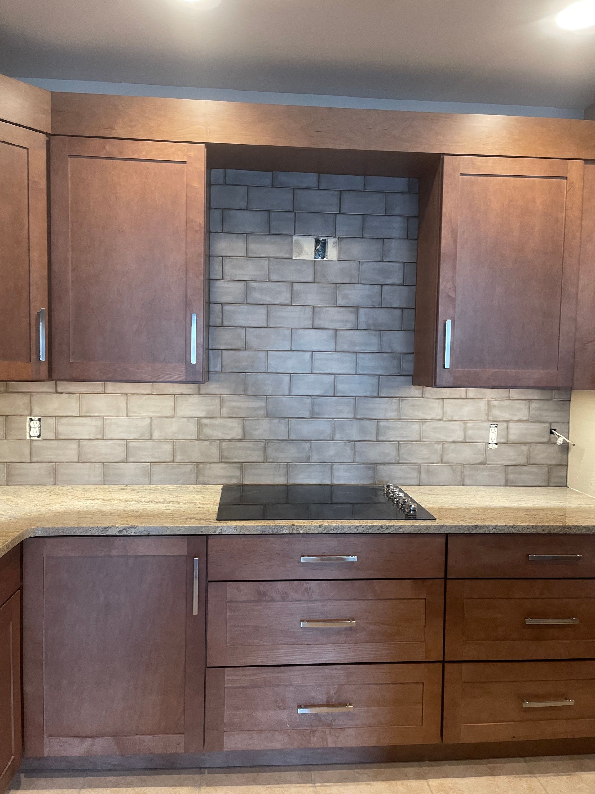 Wooden kitchen cabinets with a tiled backsplash and black stovetop under a recessed hood area