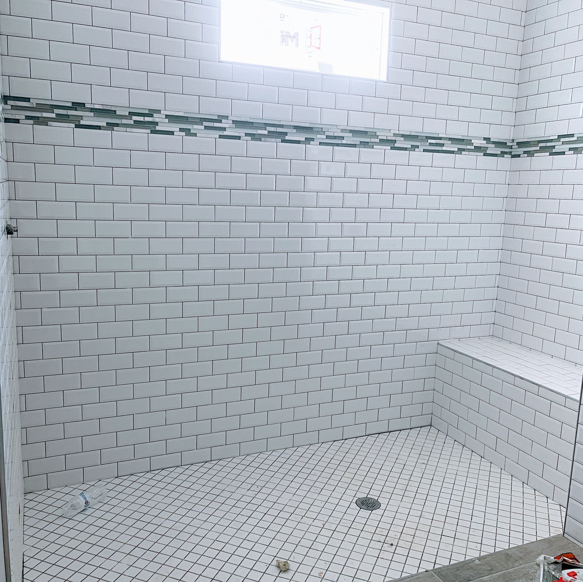 Empty white tiled shower with built-in corner shelf and floor drain