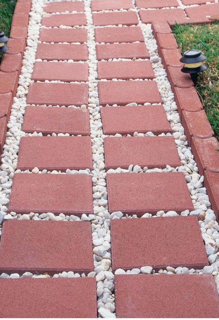 Brick walkway with white gravel between red pavers, bordered by grass and a small path light.
