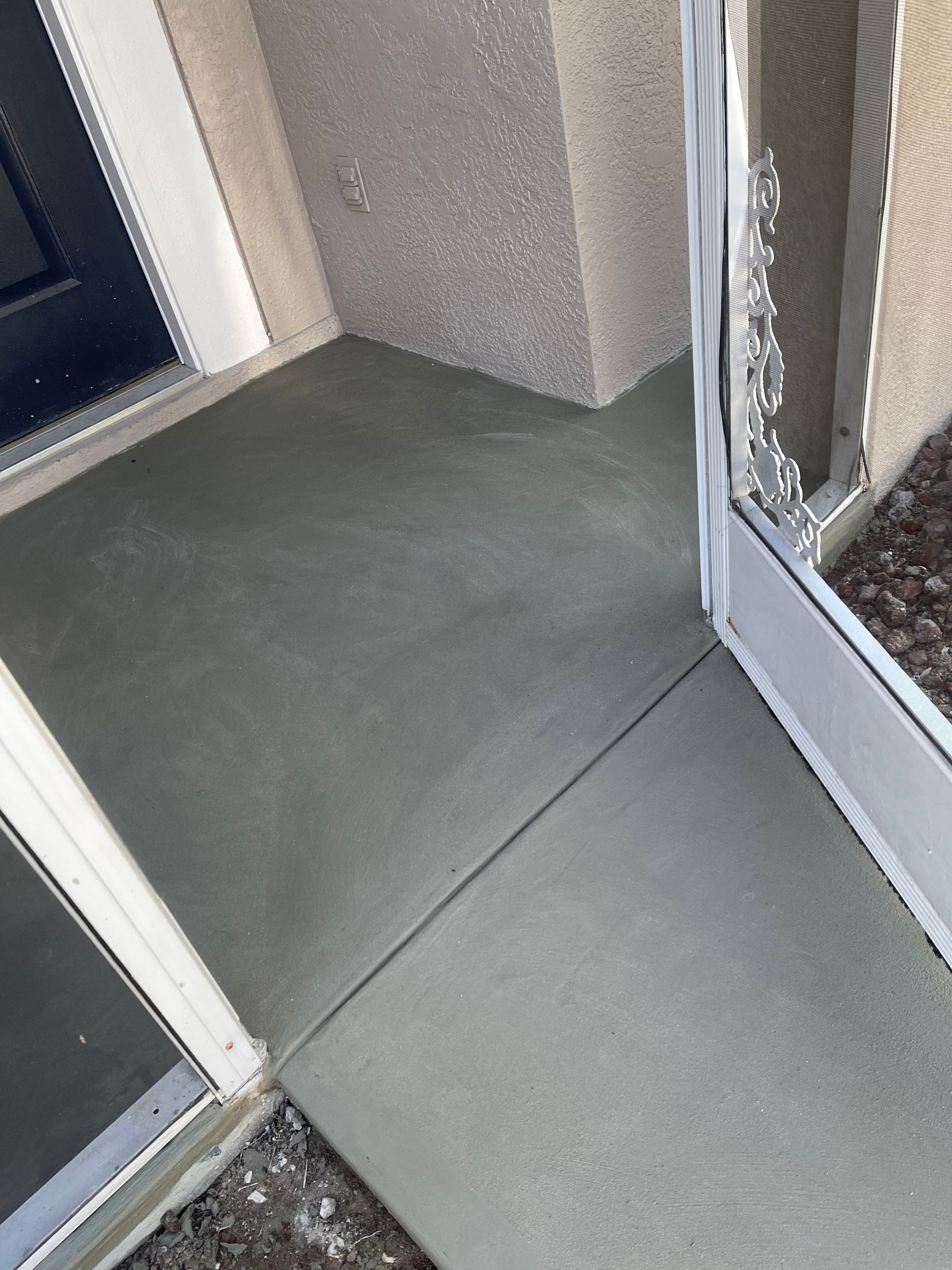 Concrete balcony walkway beside an open door and window, with gray walls and floor tiles.
