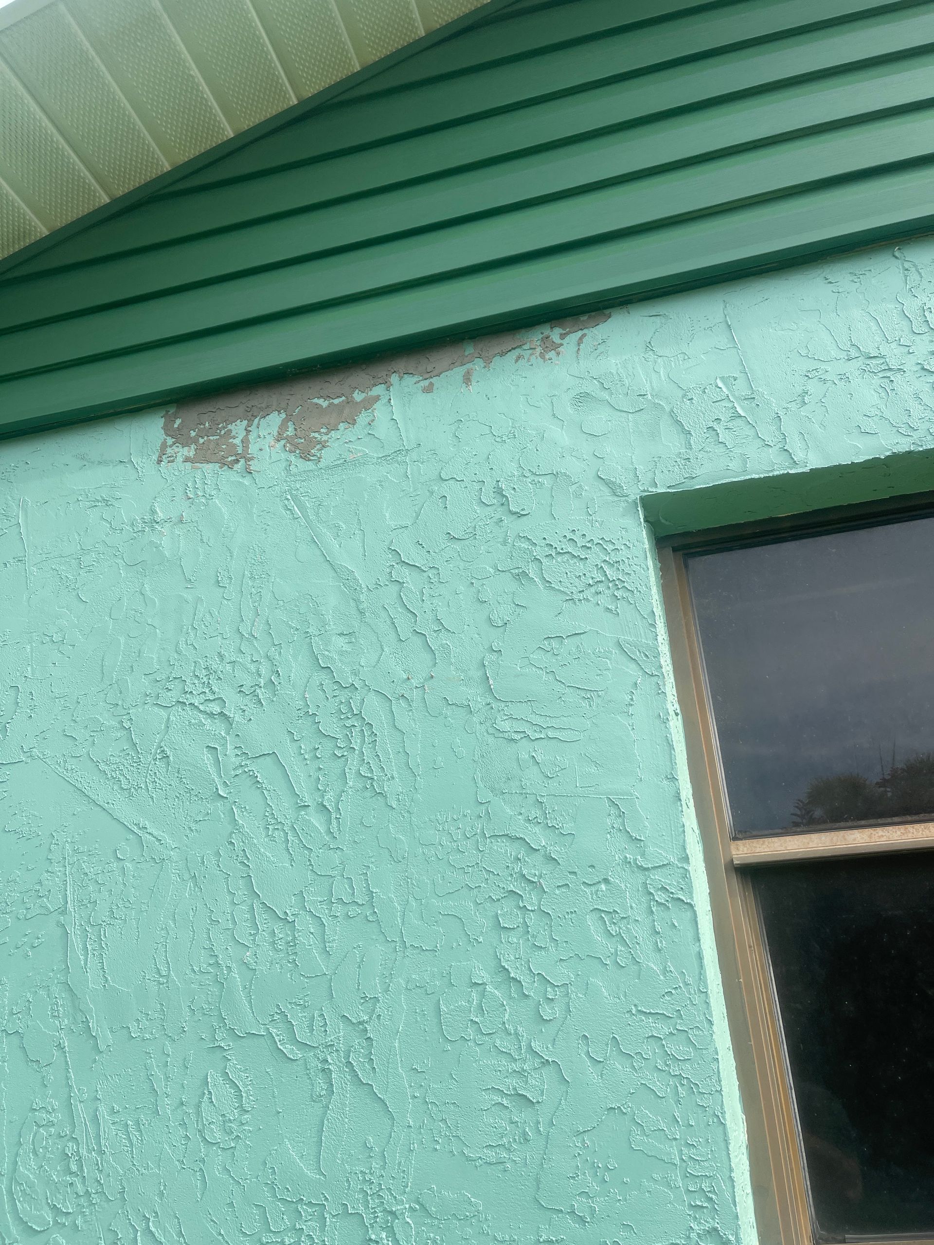 Teal stucco house wall with green siding and a window under the roof eave