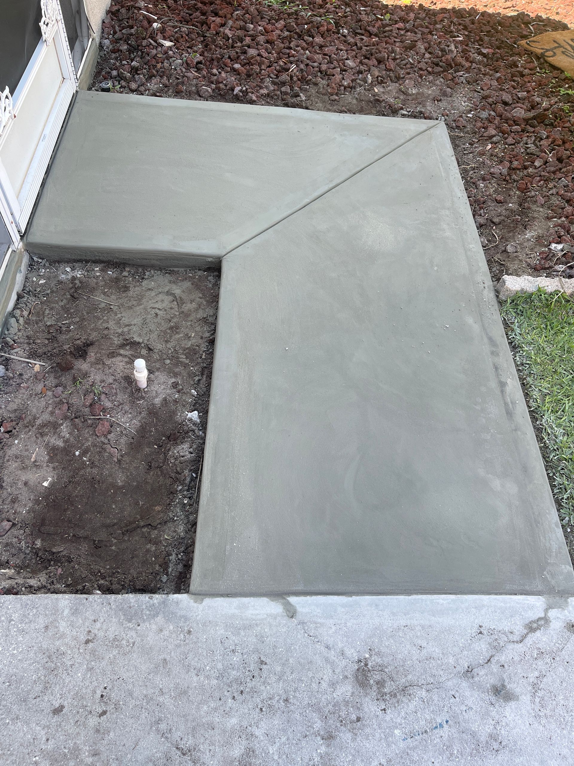 Concrete sidewalk ramp with a triangular corner beside a house and mulch bed