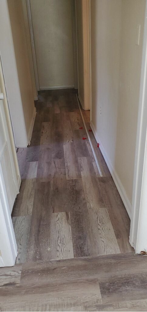Narrow hallway with wood flooring and white walls, leading to a doorway at the end.
