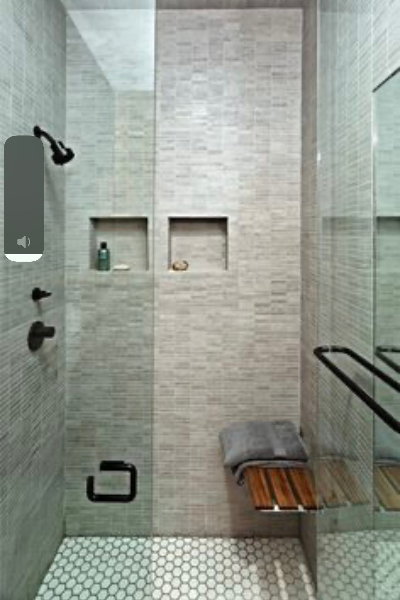 Modern walk-in shower with glass wall, black fixtures, recessed shelves, and a bench with folded towels.