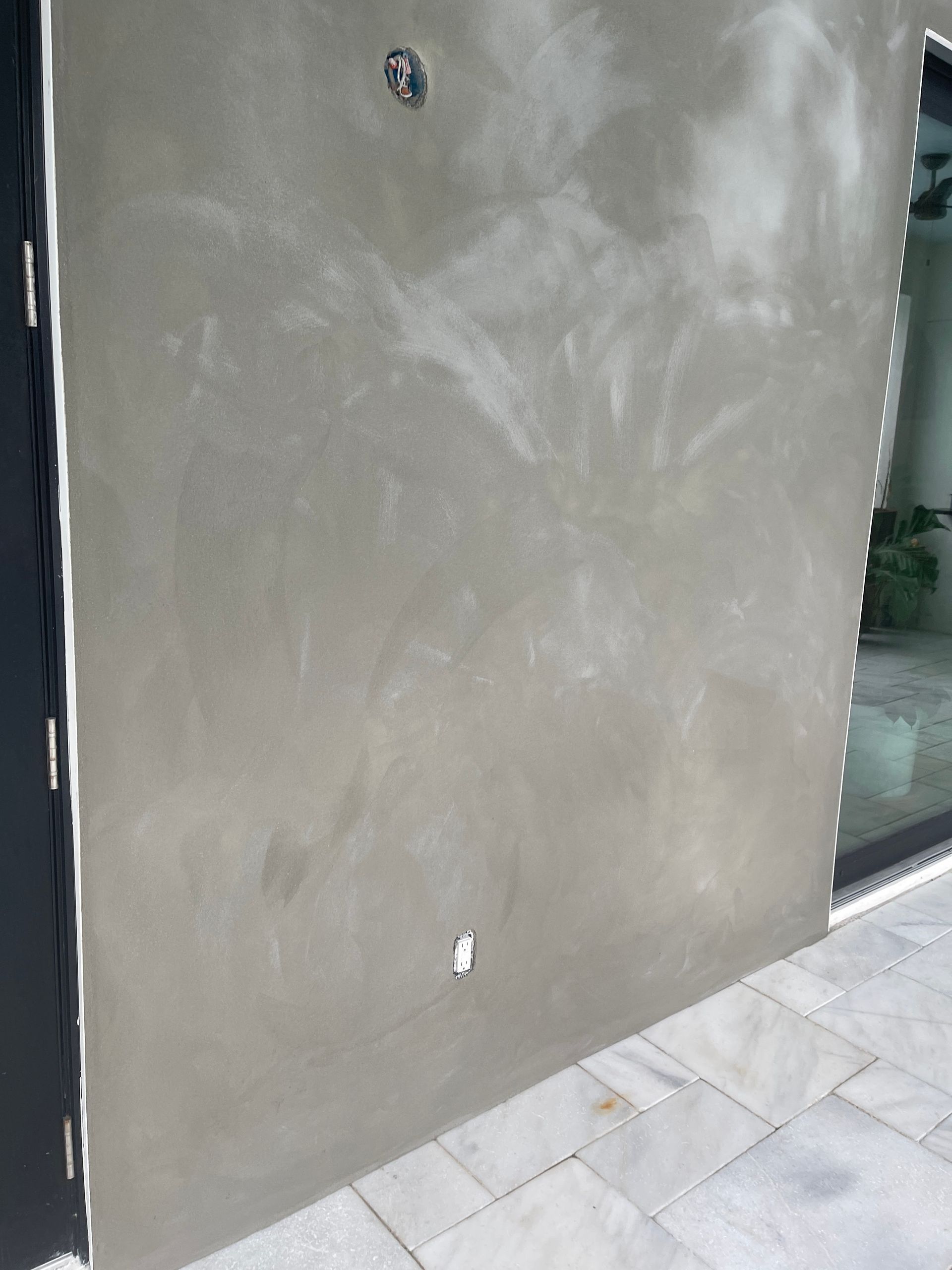Gray stucco wall beside a glass storefront and light stone sidewalk