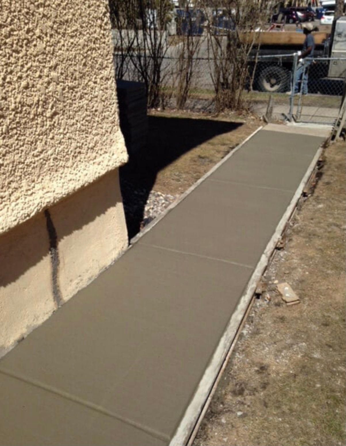 Fresh concrete sidewalk along a stucco house beside a dirt yard and street fence