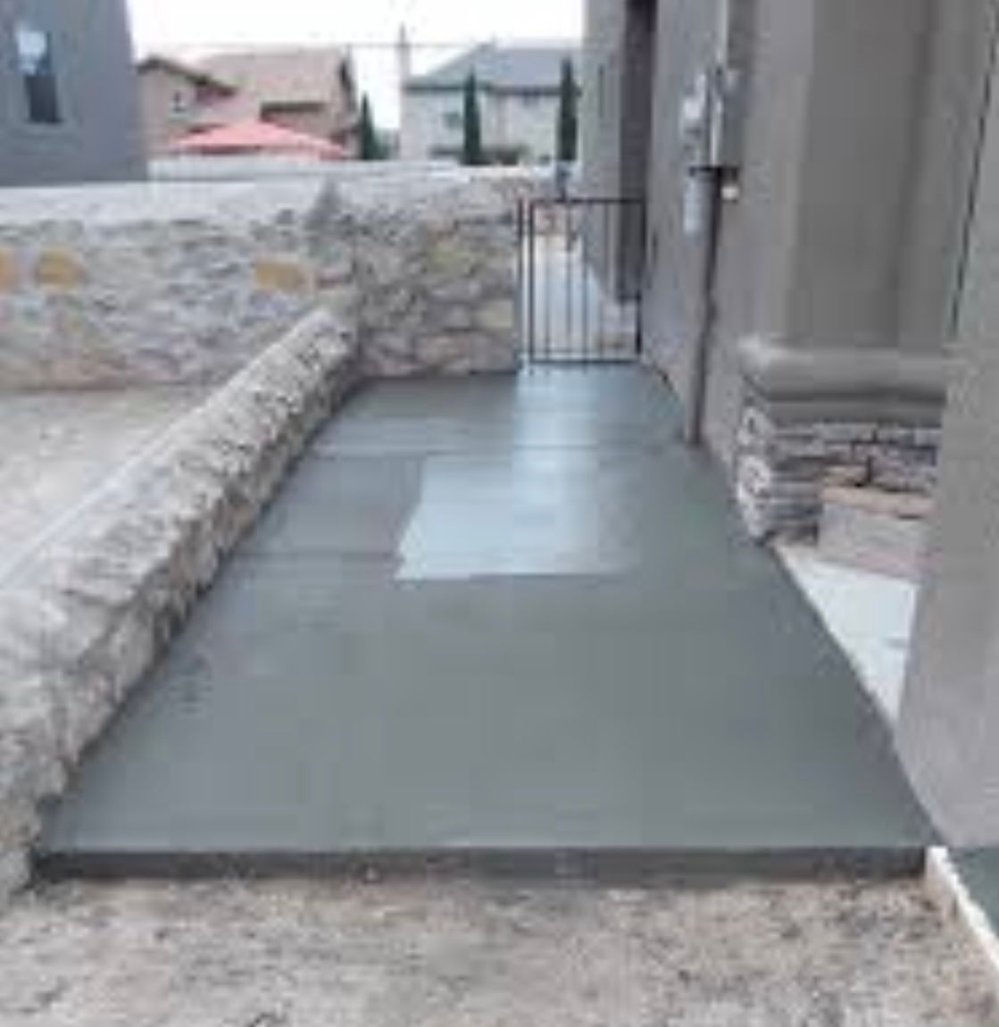 Concrete ramp walkway beside a stone wall, leading to a gate and building entrance.