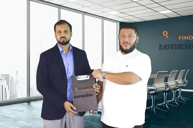 Two men shake hands in an office, holding a clipboard labeled
