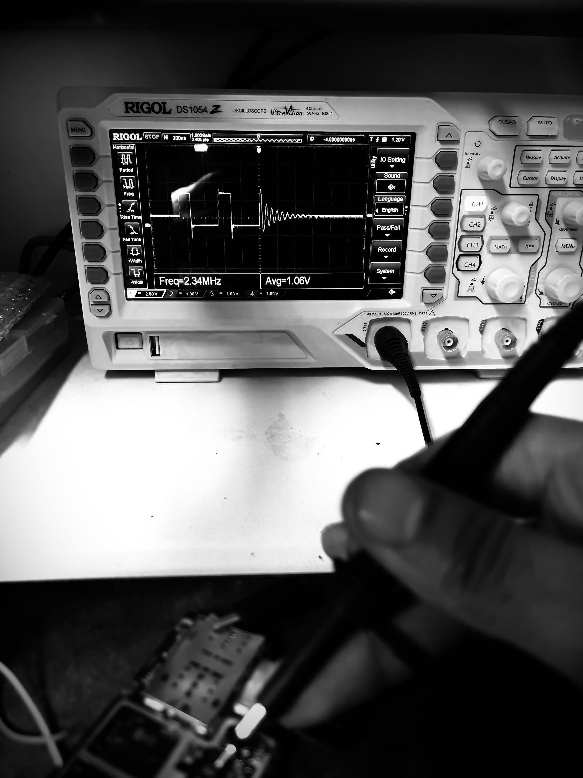 Una persona utiliza una sonda para probar una placa de circuito, y un osciloscopio muestra la señal.