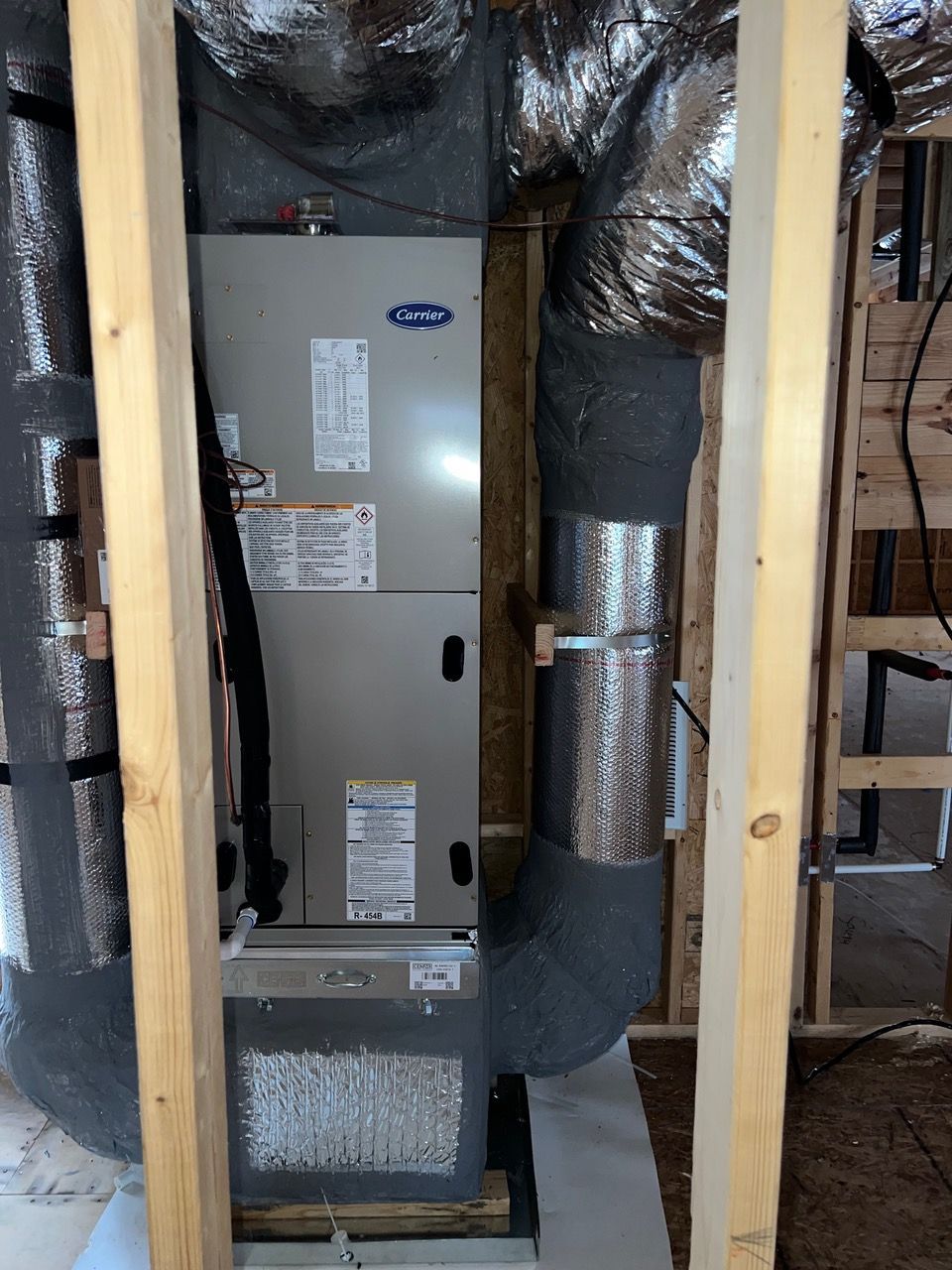 An HVAC air handler unit framed by two wooden wall studs, with insulated ducts connecting to the top and side.