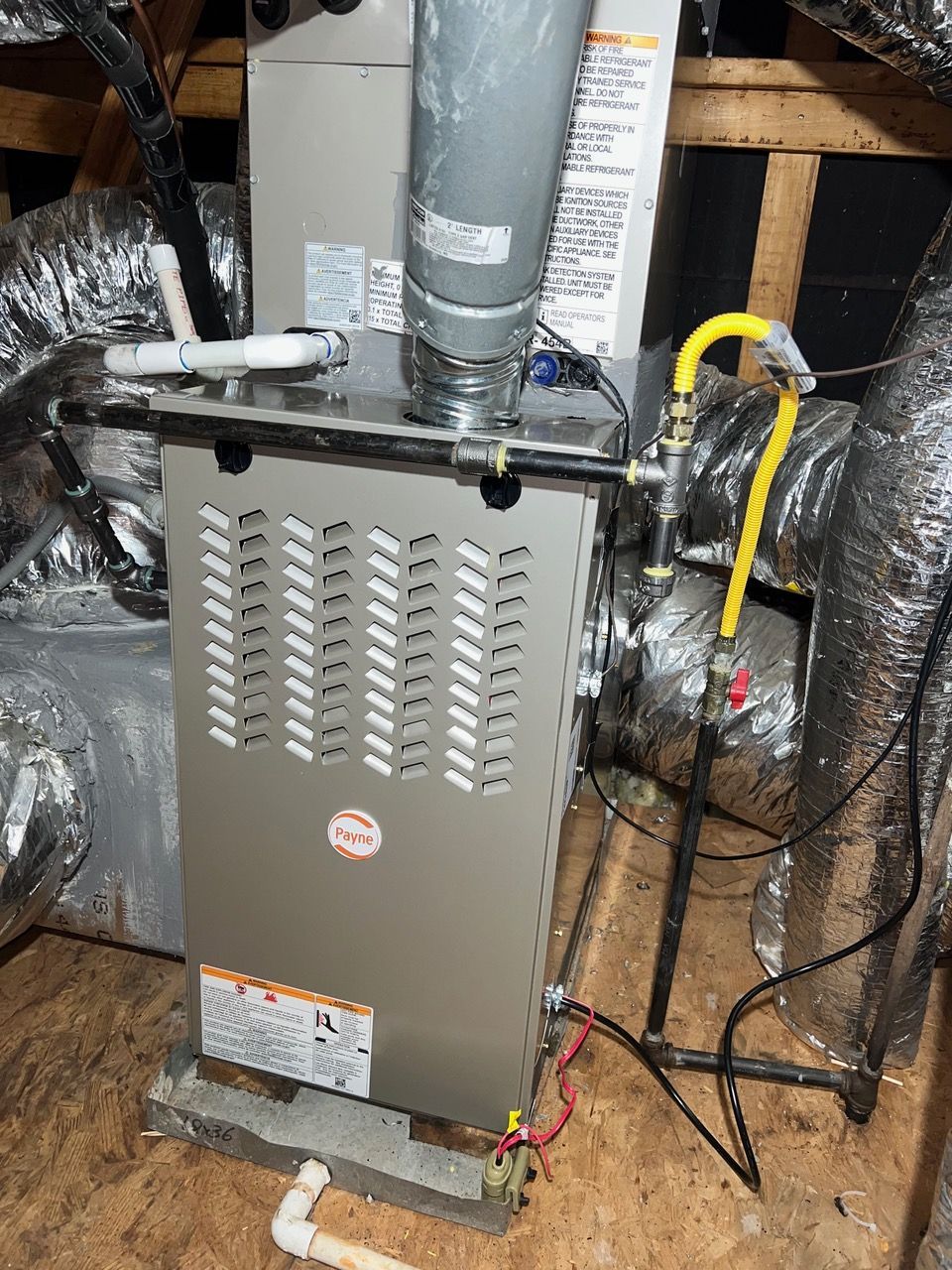 A gray residential furnace with a metal vent pipe and yellow gas line, installed in an attic space.