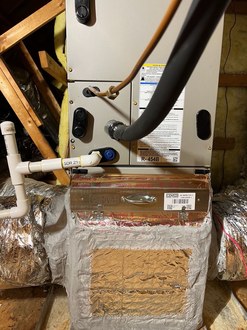 HVAC air handler unit in an attic with insulated ductwork, copper refrigerant lines, and white PVC condensate piping.