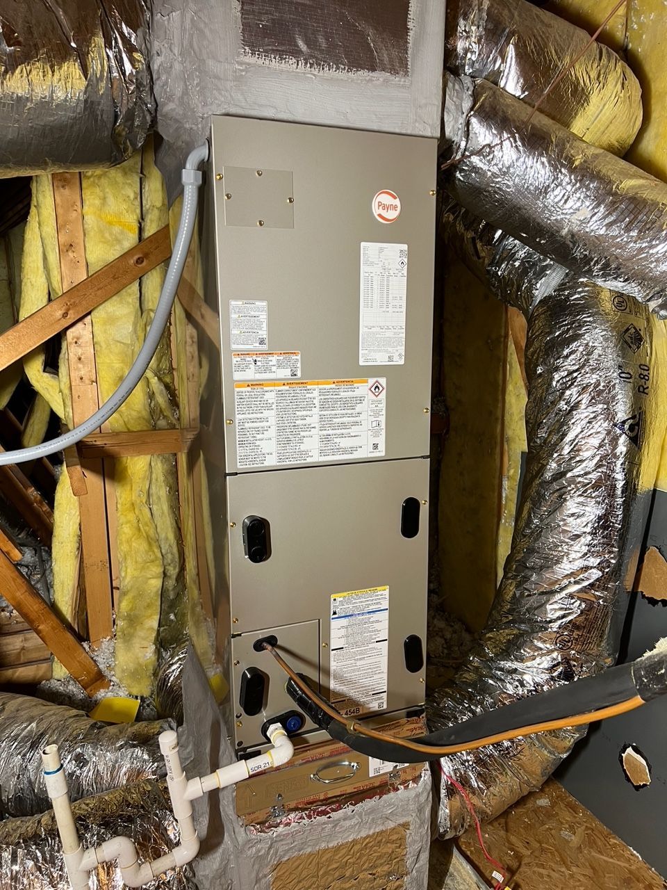A gray HVAC air handler unit installed in an attic surrounded by insulation and flexible ductwork.