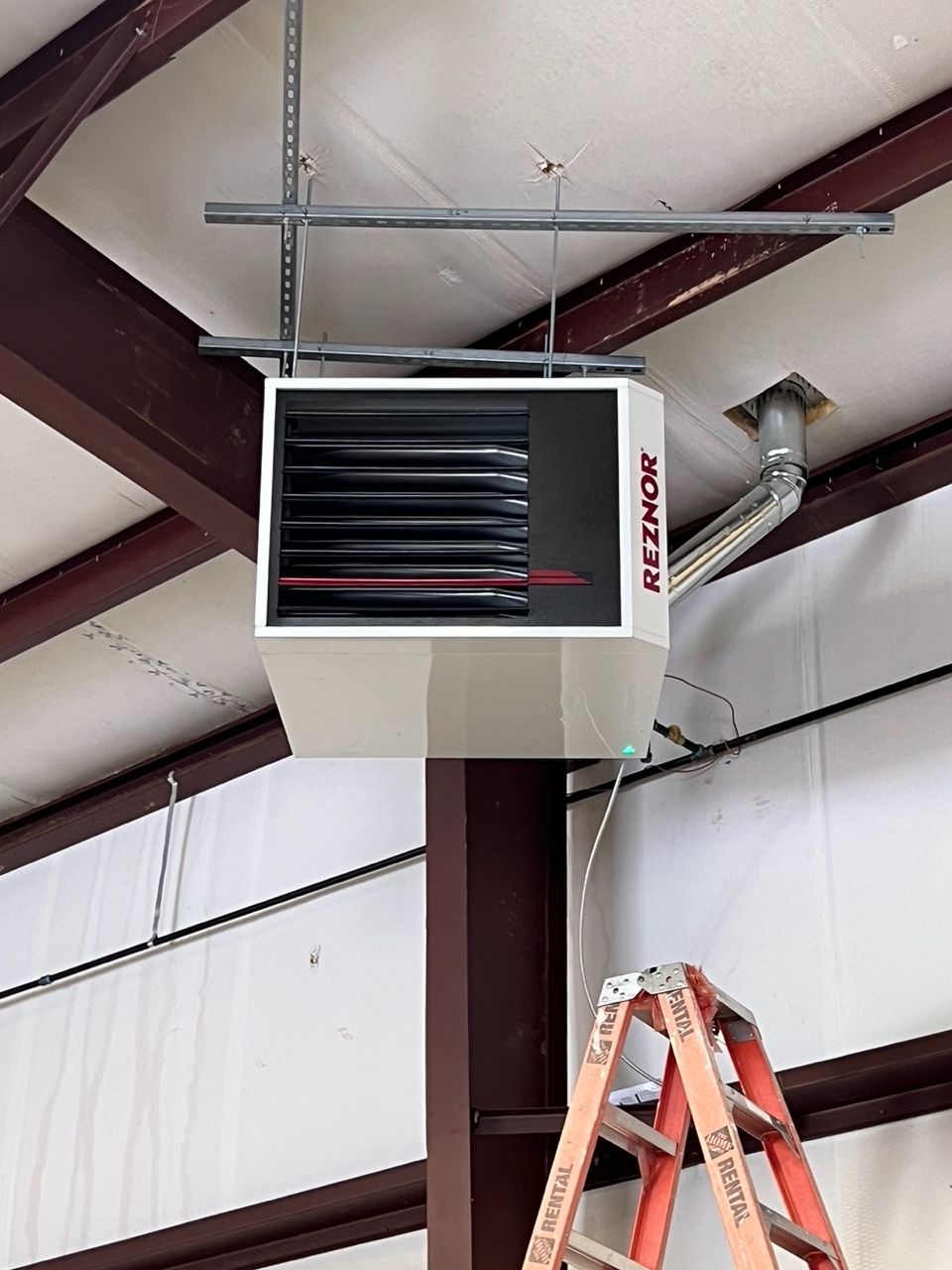 A Reznor heater hanging from the ceiling of a warehouse, with a ladder positioned below it.