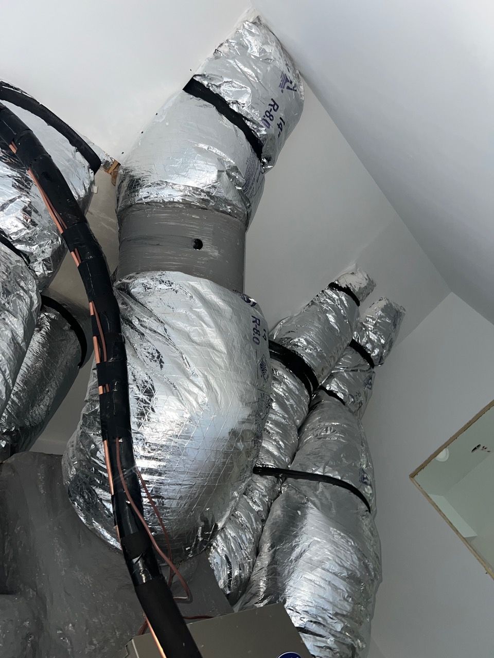 Silver-insulated flexible HVAC ductwork attached to a ceiling with a visible puncture in the central duct coupling.