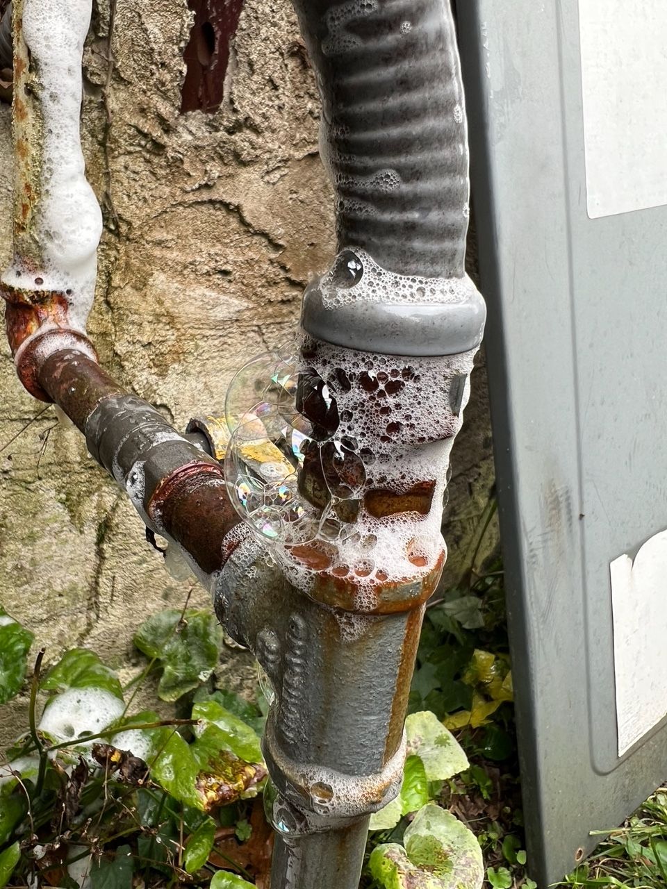 A close-up of a corroded metal pipe joint with bubbling soapy residue, indicating a detected gas leak.